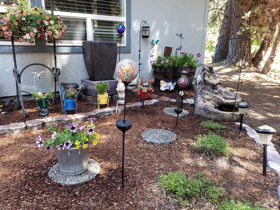 A peaceful little flower bed with beautiful flowers, fountains, rocks, and decorative objects on a sunny summer day.