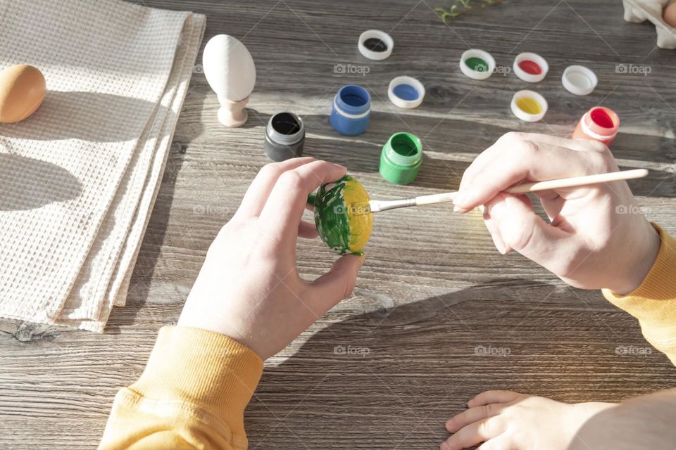 A little son and his father together in their free time paint Easter, chicken eggs with paints and brushes for the holiday.  A child and a man create a craft and natural product in their family business.