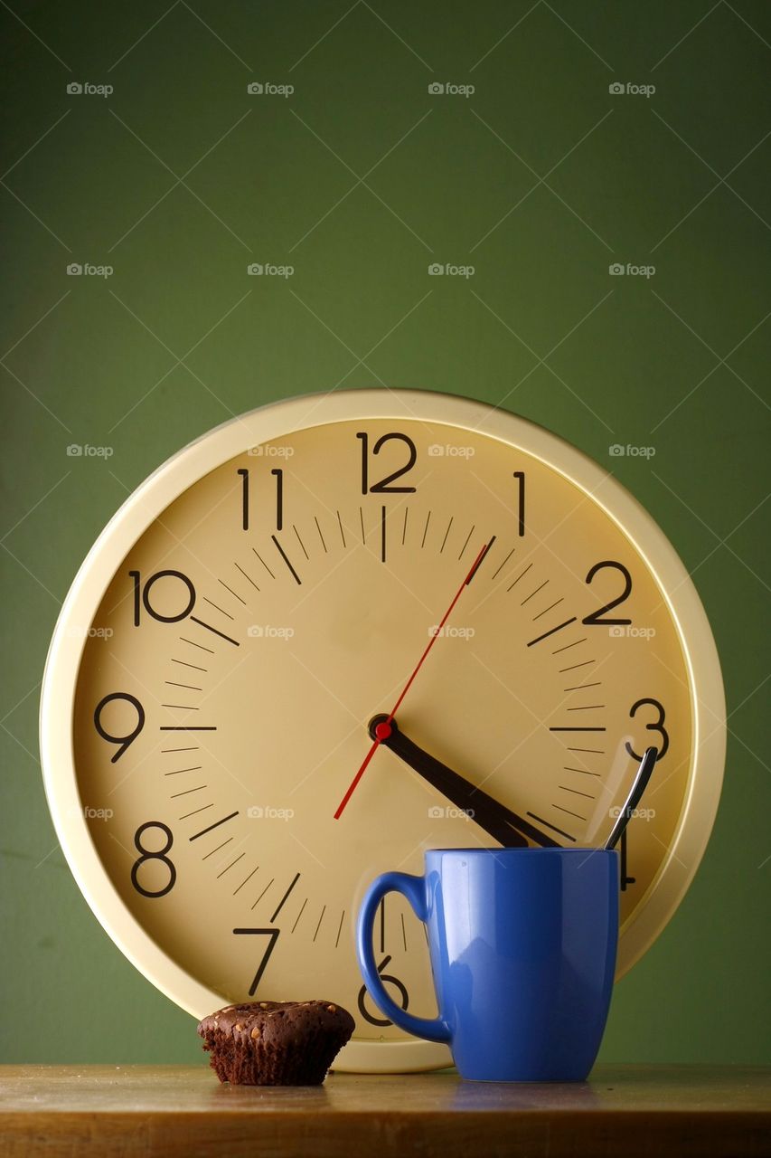 blue coffee mug with teaspoon, a brownie and an analog clock
