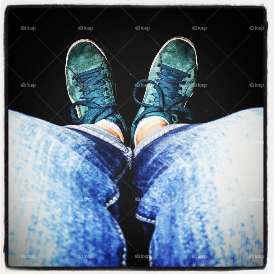 Person sitting wearing blue jeans and green sneackers. Black background.