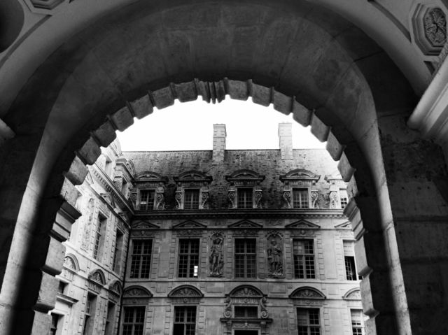 Arched walkway into courtyard. Buildings surround courtyard -- entry through large stone Arch. 