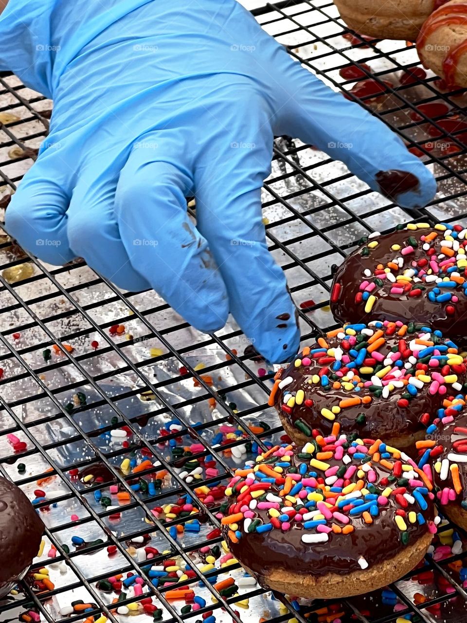 Blue gloved donut maker selecting my favorite just made chocolate-and-sprinkles covered donuts at the outdoor Farmer’s Market 