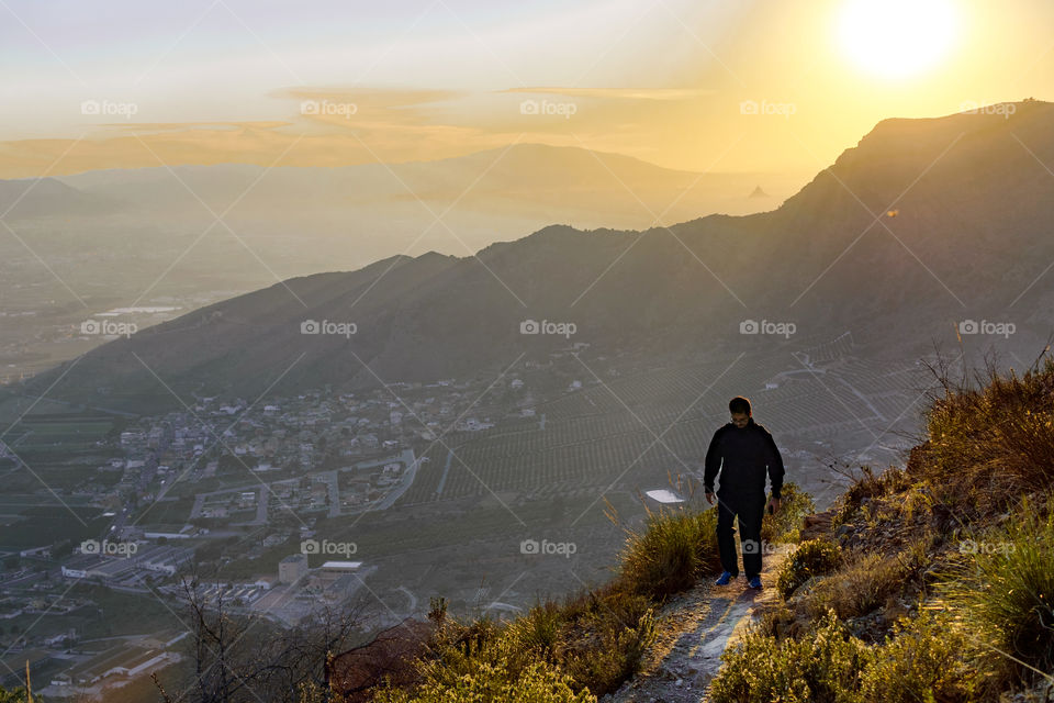 Sportman hiking at the top of a cliff against cityscape and sunset