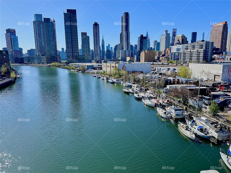 This is “Newtown Creek”, an ocean inlet of the “E River” with its variety of boats seen from the “Pulaski Bridge” that connects LIC to “Greenpoint”, Bklyn. In the distance we see “Manhattan” incl. the “Empire State Bldg”. 2024. Hypnotic Productions