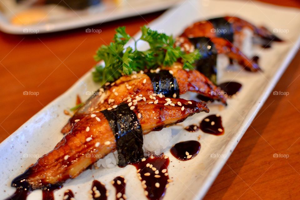 Fresh sushi  eel roll with a sweet sauce drizzled on top on a plate with garnish