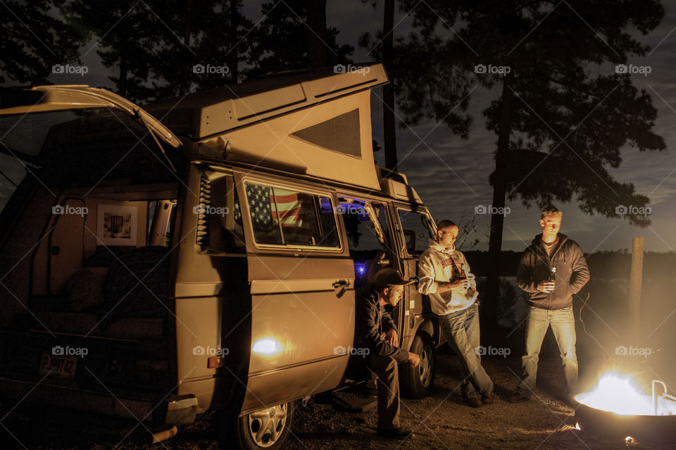 Group of men standing near campfire drinking beer