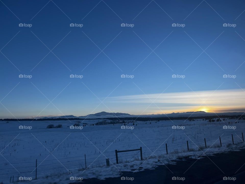 A shining sunset over a snow covered pasture and a grand mountain looming in the distance. 