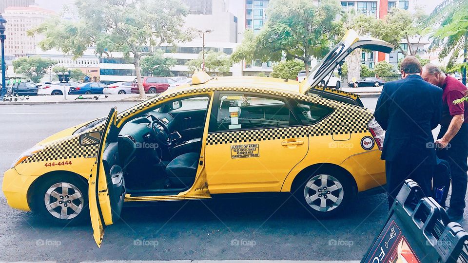 A taxi driver helps his passenger load luggage into the trunk of the taxicab