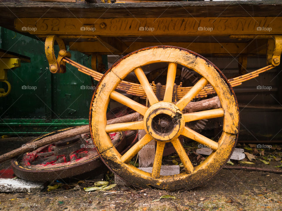 Old and rusty, yellow wagon wheel on suspension.