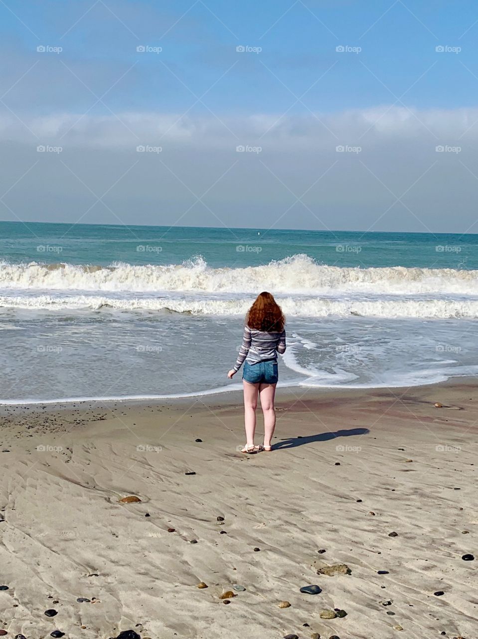 Beautiful redheaded model walking along the beach in the early morning near the crashing waves