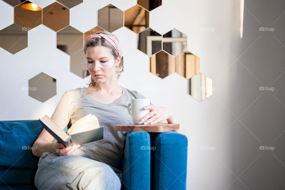 Young woman reading a book, drinking coffee with eye patches