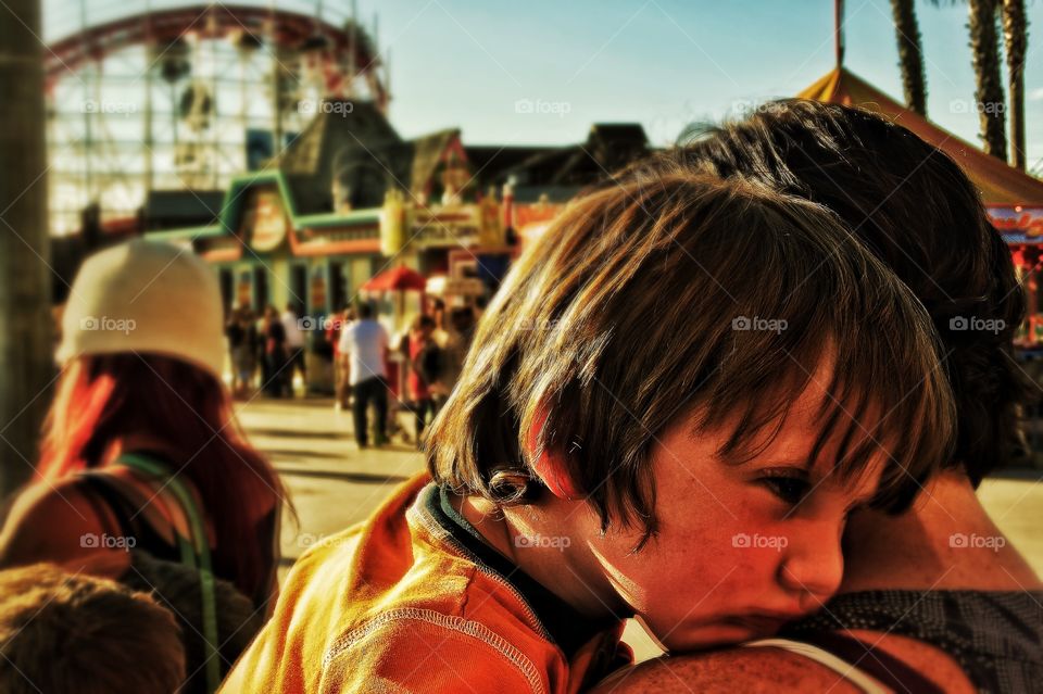 Sleepy Boy During Golden Hour. Toddler Resting His Sleepy Head On Mom's Shoulder At Sunset After A Long Day At Amusement Park
