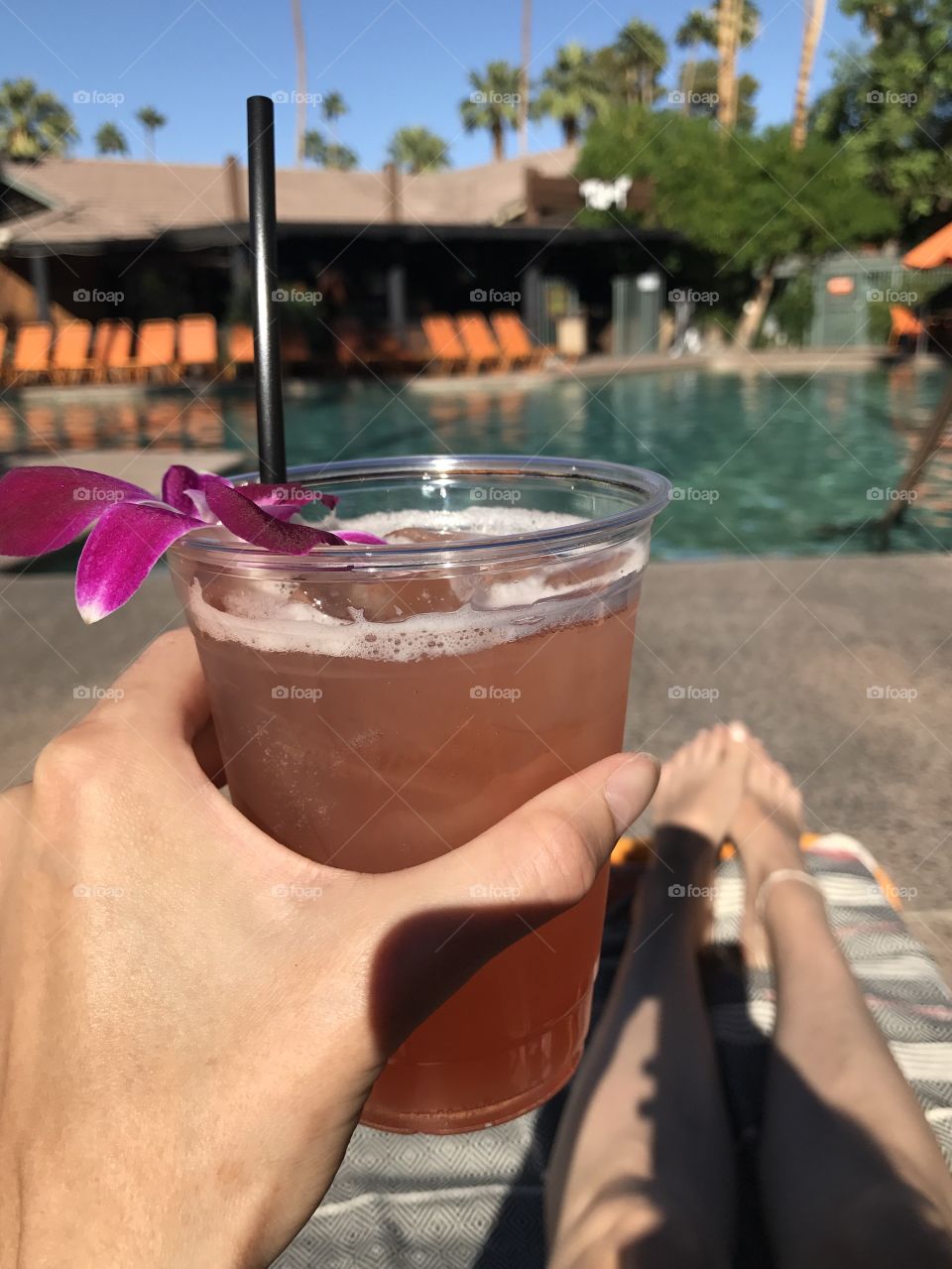 Cheers! A tropical cocktail by the pool. Having a drink in the sun. Pink cocktail with flower. California holiday.