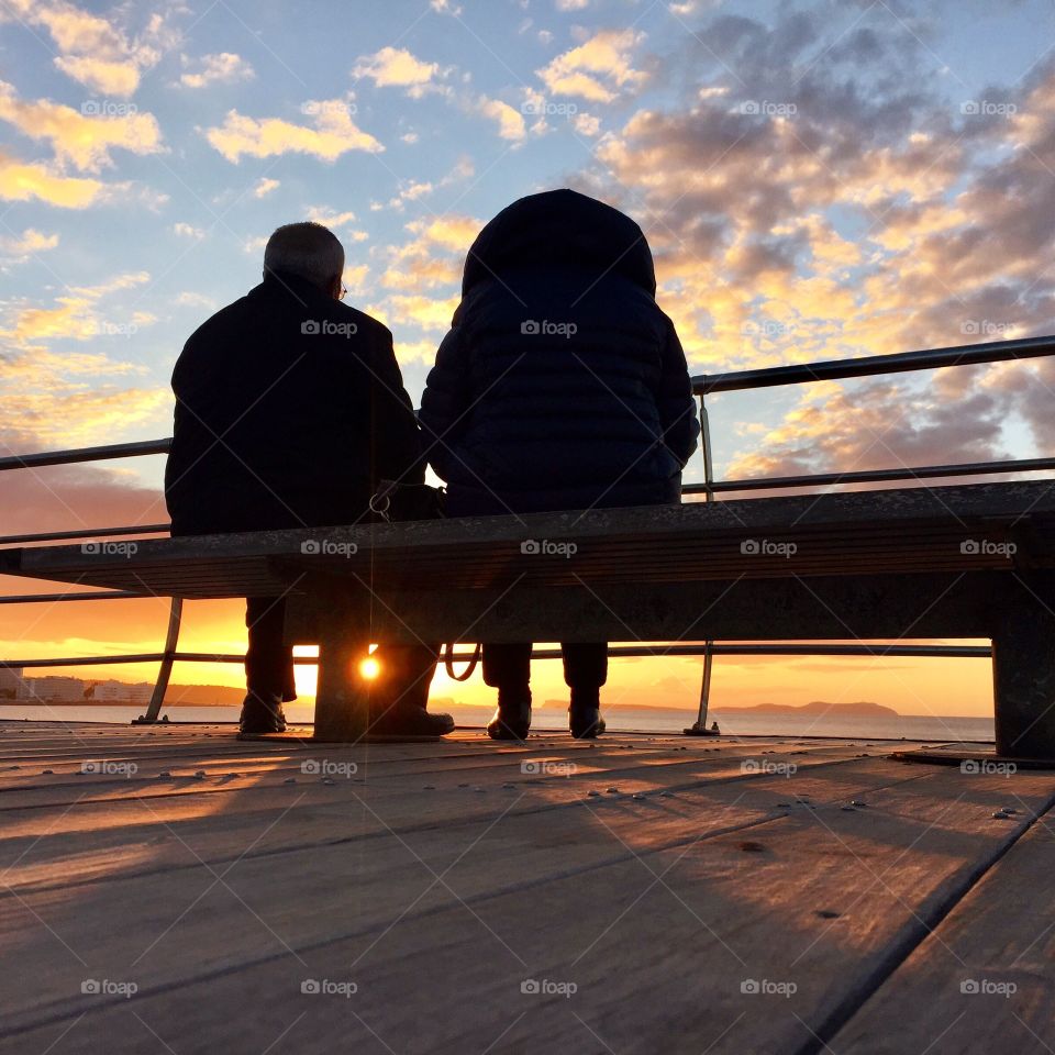 Couple sitting on the bench and watching sunset 