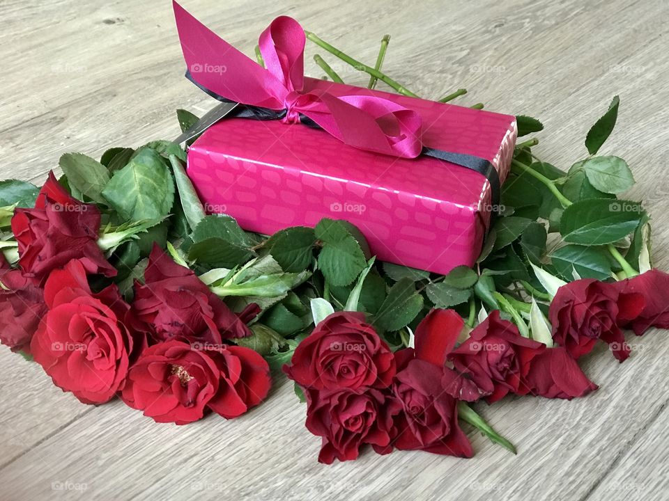 A bouquet of red roses and a pink gift box, wooden background 