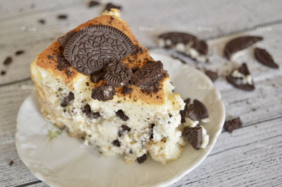 Oreo cookie cheesecake on a white plate with a white rustic background and cookie crumbles in the background