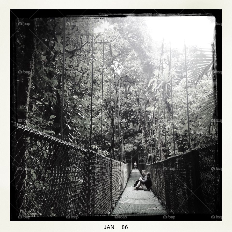 Two people take a break halfway across a suspension bridge in the cloud forest of Monteverde, Costa Rica.