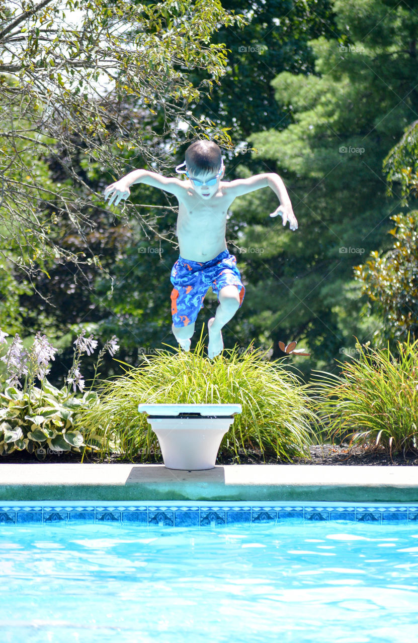 Young boy jumping off of a diving board into an inground pool