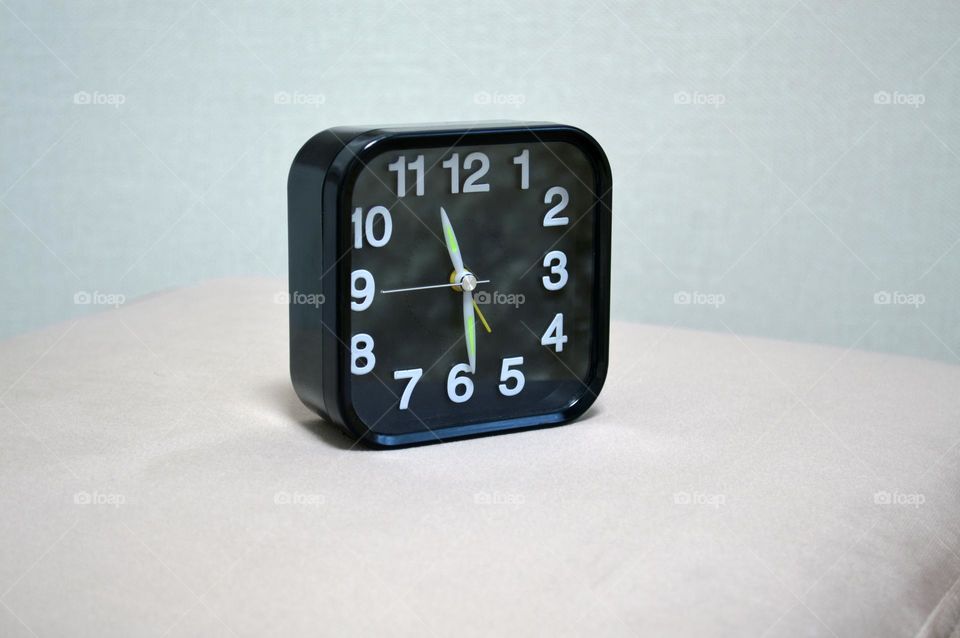 a black clock sits on the ottoman by the bed in the bedroom