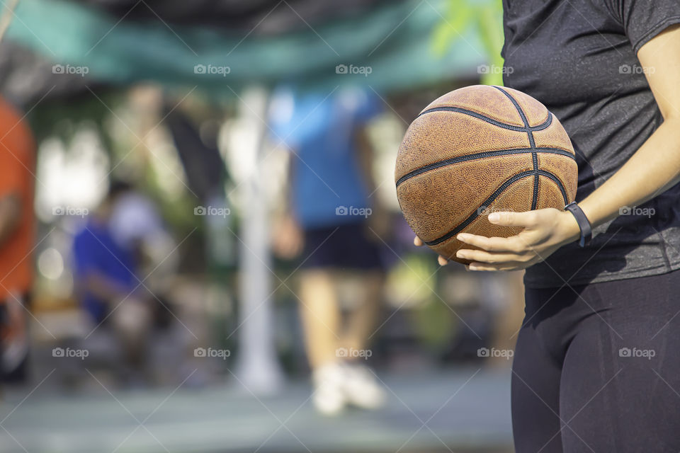 Leather basketball in hand of a woman wearing a watch Background blur tree in park.