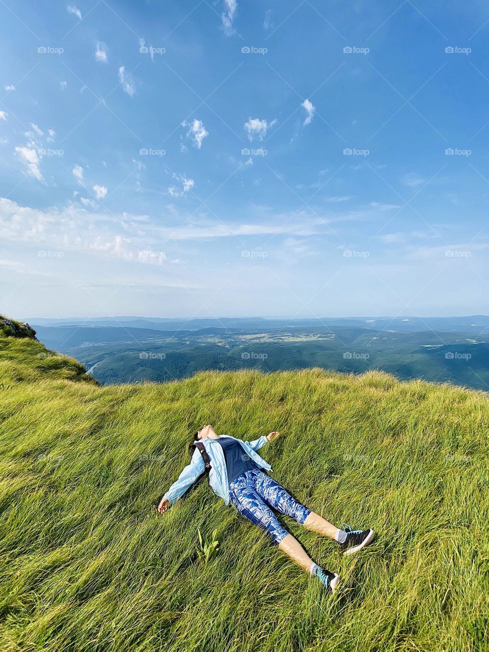 Woman lying in green grass at the hill. Village.  Meadow.  Spring travel.  Happy lifestyle.