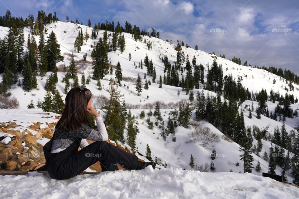 Girl is sitting on the edge of the snow path  and enjoying the peaceful view of mountains landscape 