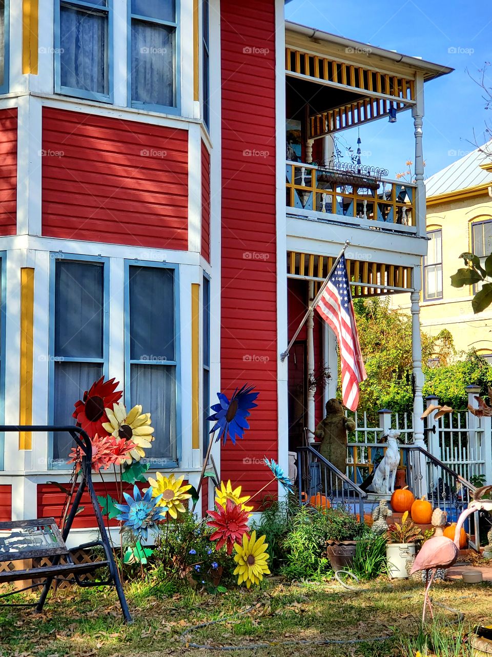 Colorful historic home with a second b floor balcony, yard art and the American flag