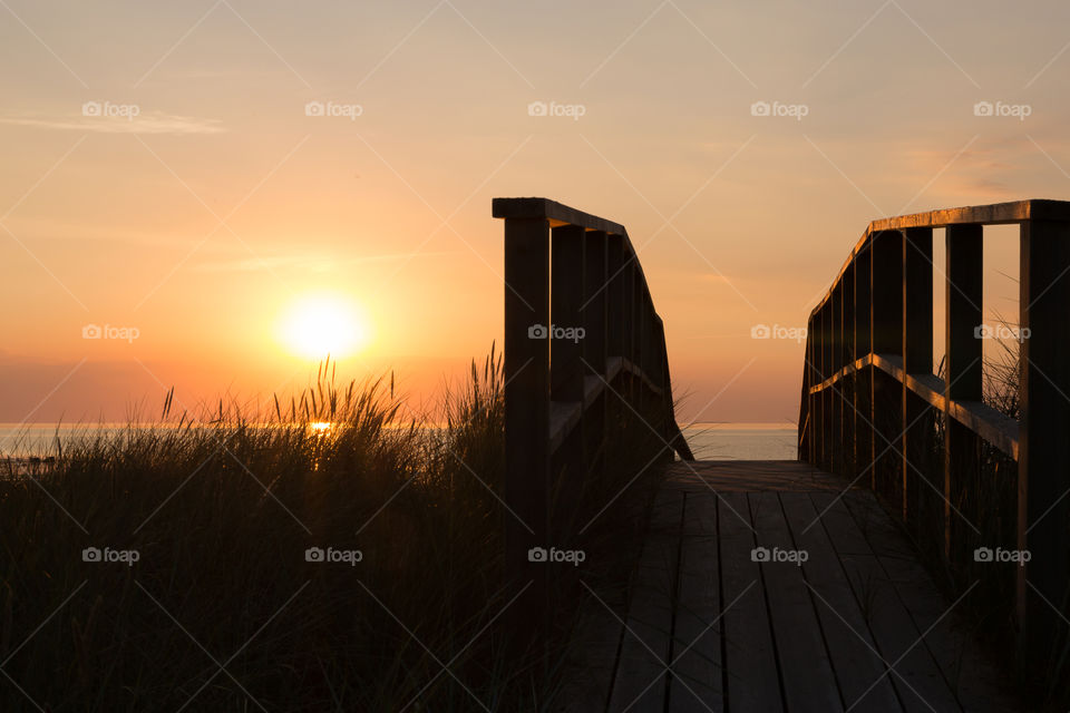 Sun shining on wooden boardwalk at beautiful orange colored sunset by the ocean 