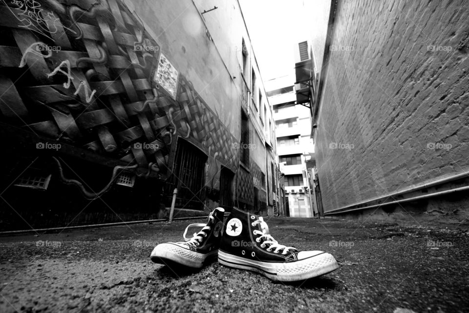 black and white image of genuine original converse all-star high tops in the foreground of a back alley in Perth, Western Australia