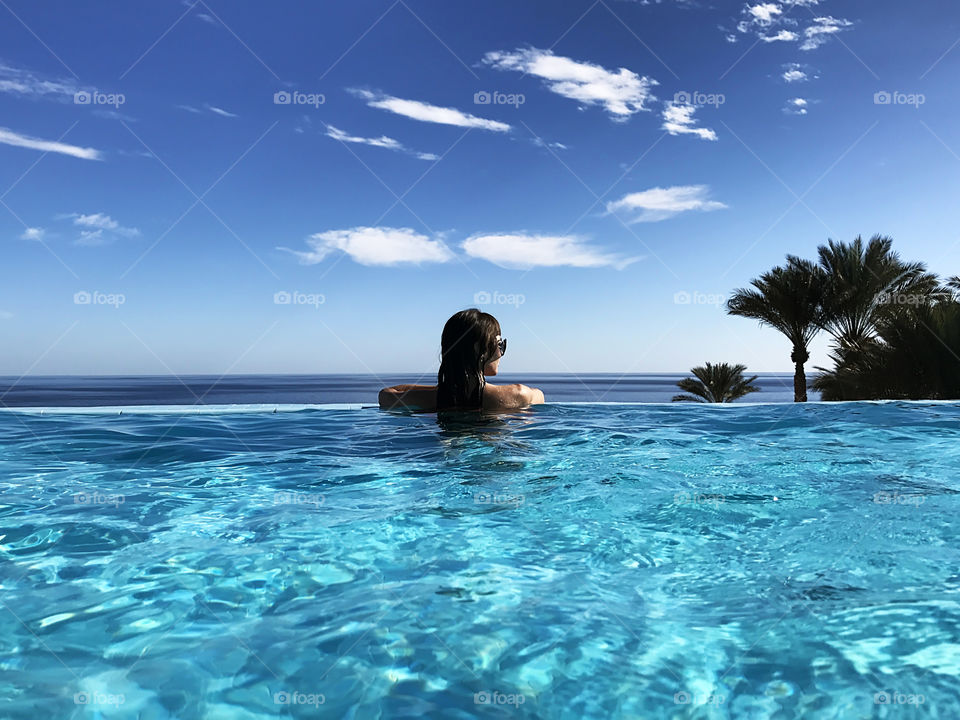 Young woman enjoying her tropical vacation at the swimming pool and amazing view above the sea 