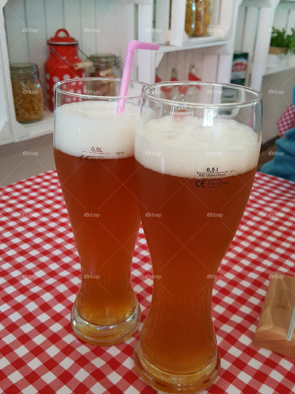 Two lager beers in glasses with a straw standing on a checkered tablecloth