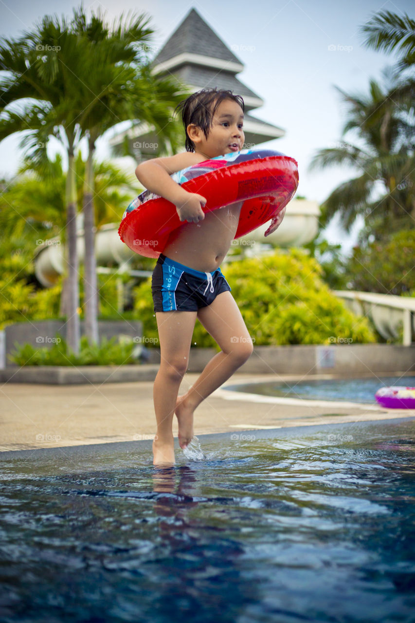 young happy boy ready to jump in the pool at a resort on a hot sunny summer day