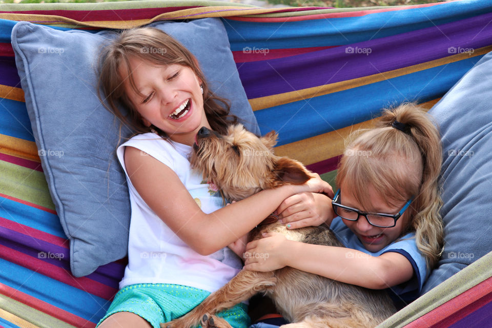 Two girls cuddling with their dog in the hammock