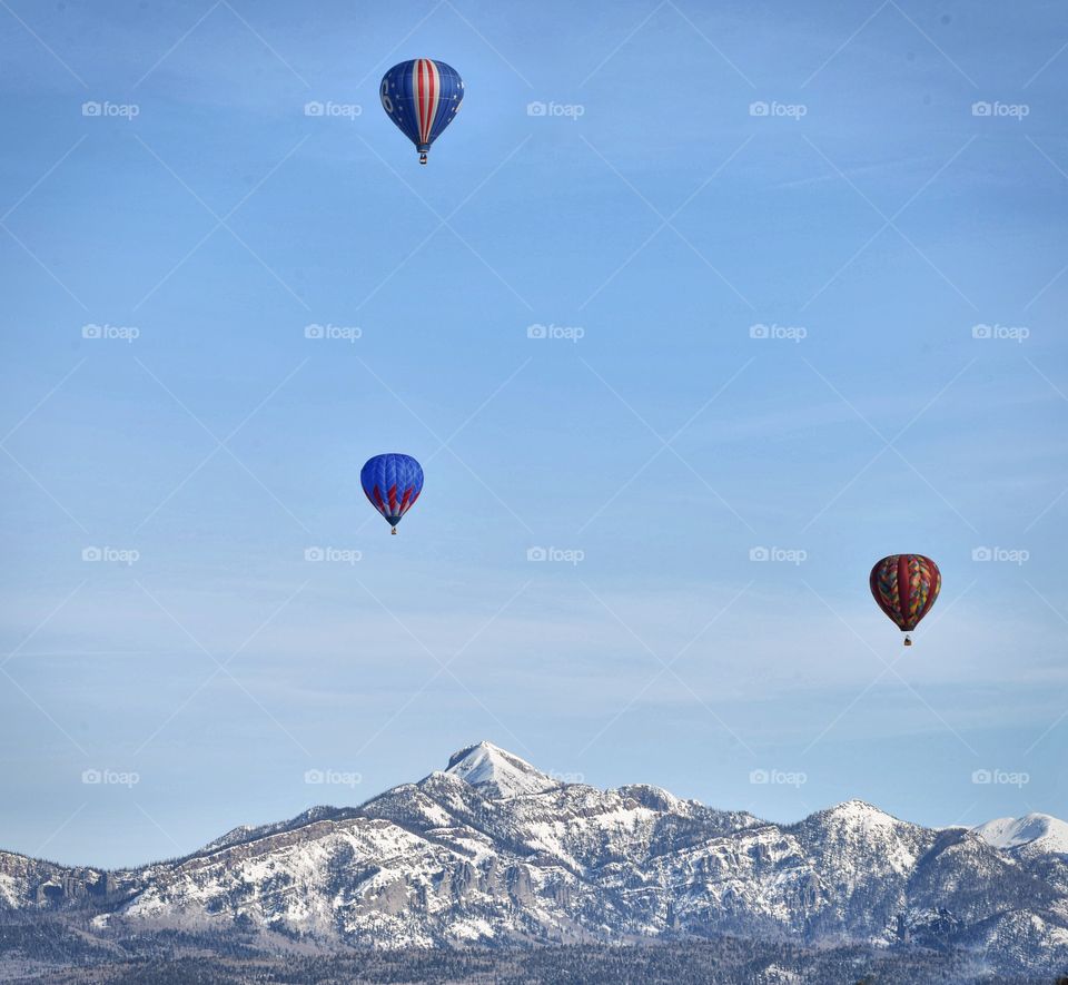 A hot air balloon festival in the winter creates a colorful scene. A pointed peak sets the scene.