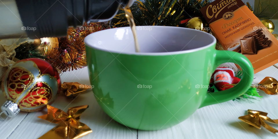 pouring tea from a thermos into a green cup on the background of a Christmas toy