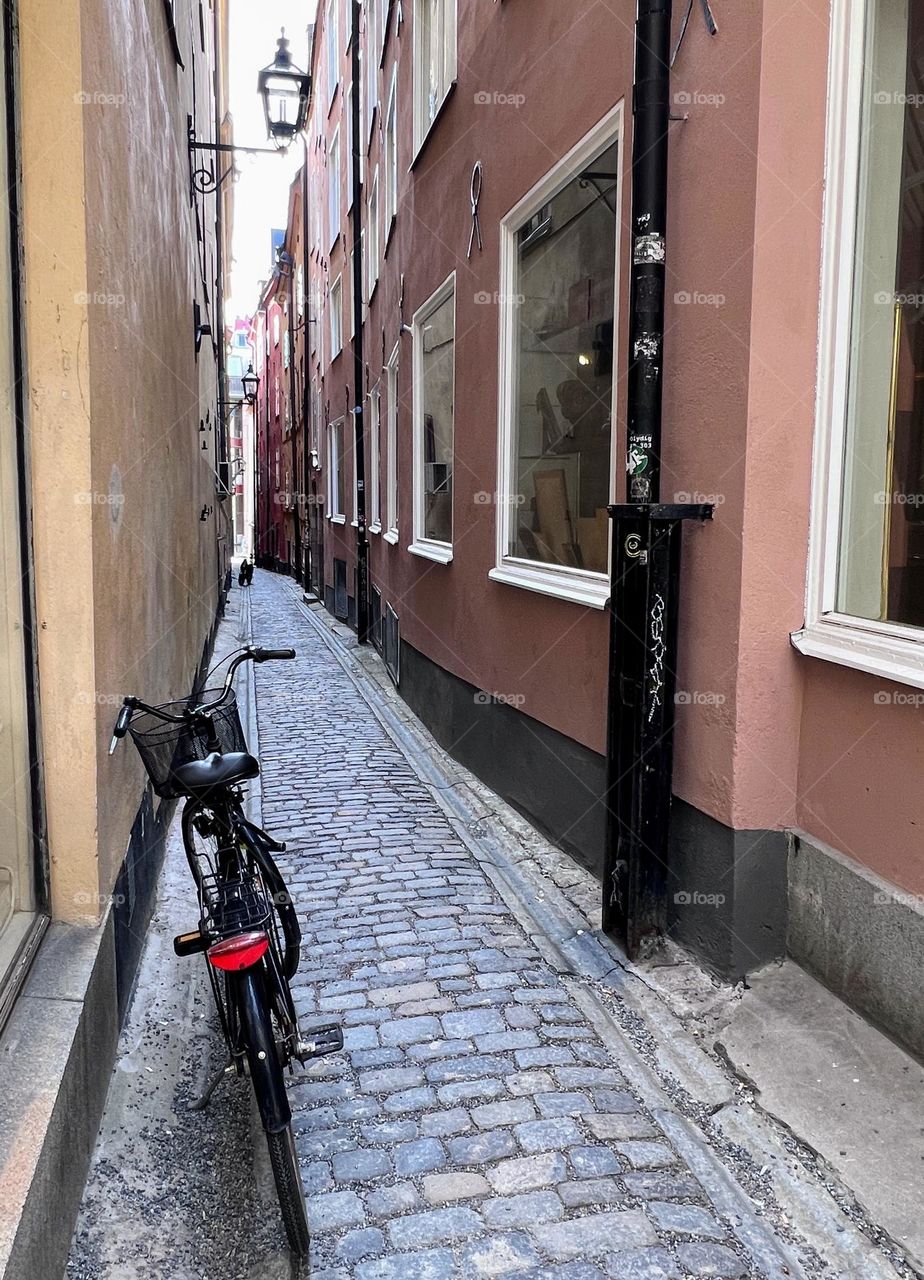 One lonely bicycle with the basket on the narrow paved curved street between two buildings 