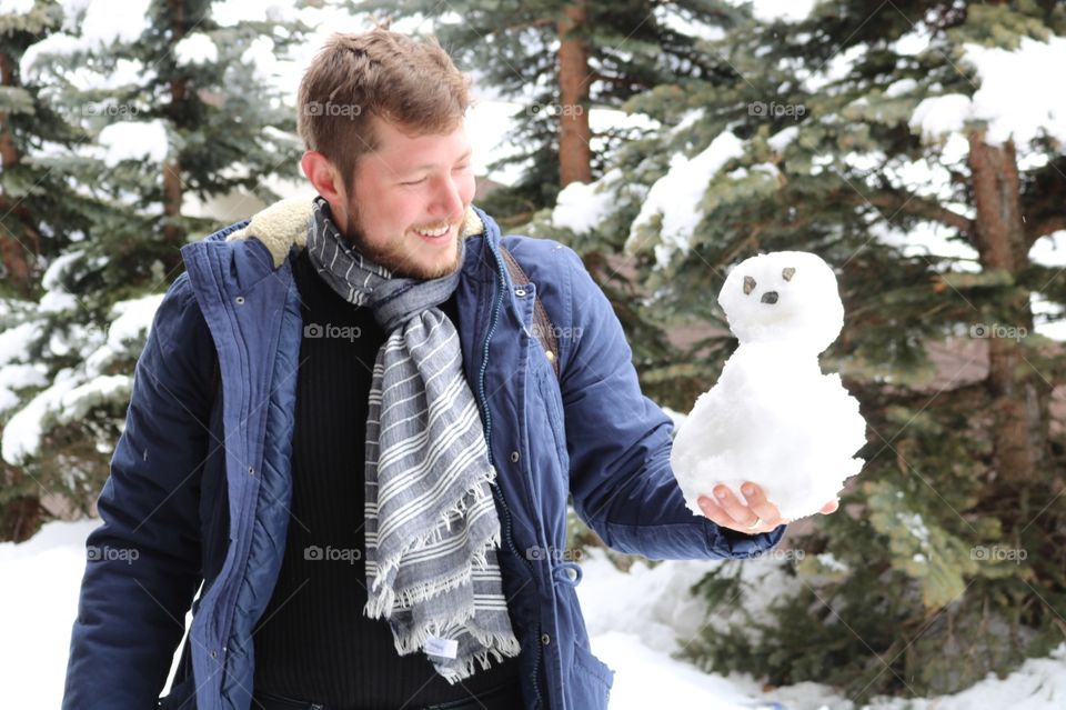 Belo homem loiro com seu boneco de neve em um clima de inverno europeu 