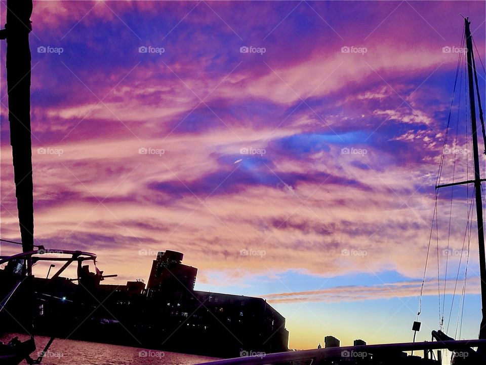The dark outline of a factory bldg on the Greenpoint, Bklyn side of the E River at Newtown Creek, LIC. Queens, can be seen on a late 2021 evening offset against the colorful clouds in the sky reflecting the setting sun’s rays. Hypnotic Productions