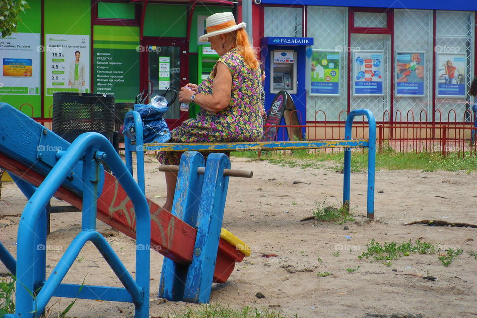 an elderly woman is sitting on a bench near a playground