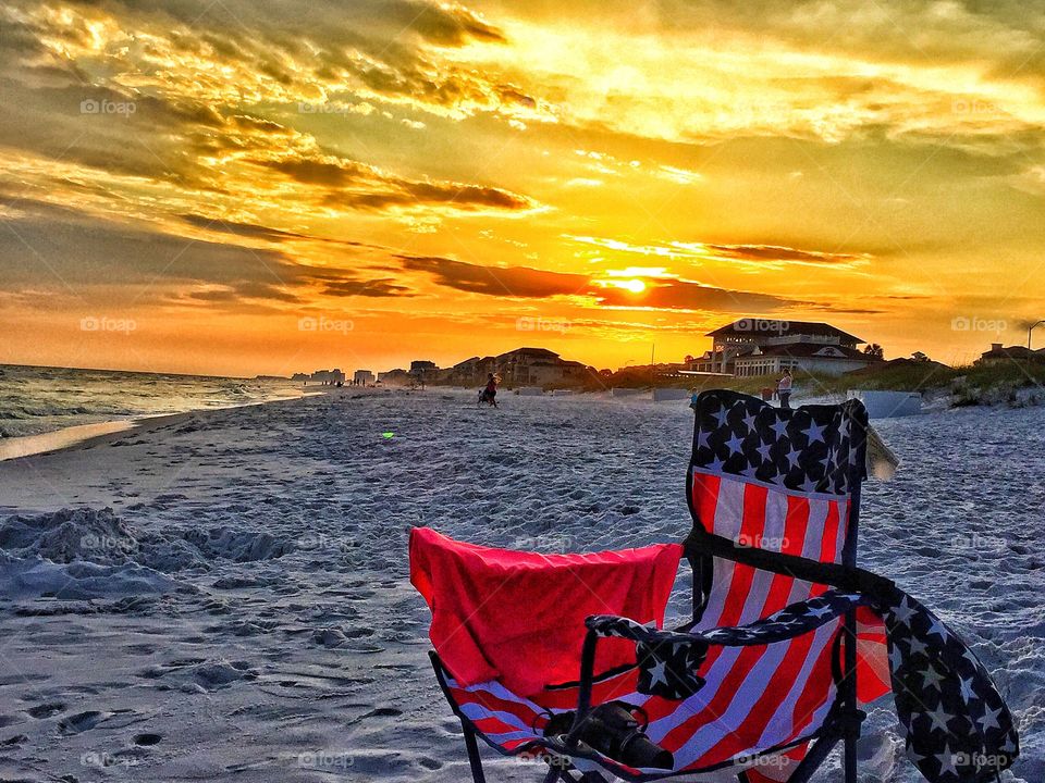 Red, white ,  and blue chair at the beach during sunset