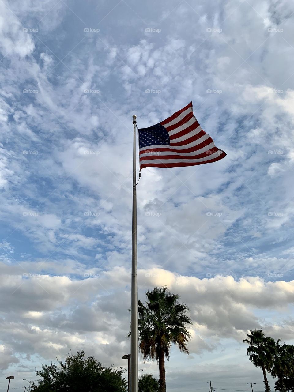 The blue sky is filled with scattered and massive clouds as the United States flag blows in the wind