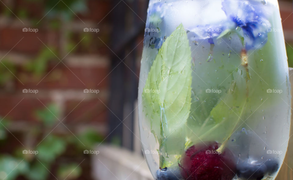 Frosty glass of refreshing flavored water with mint, lime juice, cherry and blueberry garnished with floral ice cubes of pansy edible flowers for healthy refreshing summertime drink