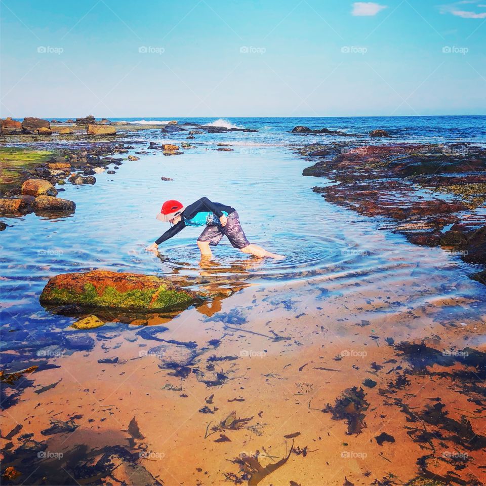 Boy with bright red hat in rock pool in Sydney on a sunny day in Sydney Australia 
