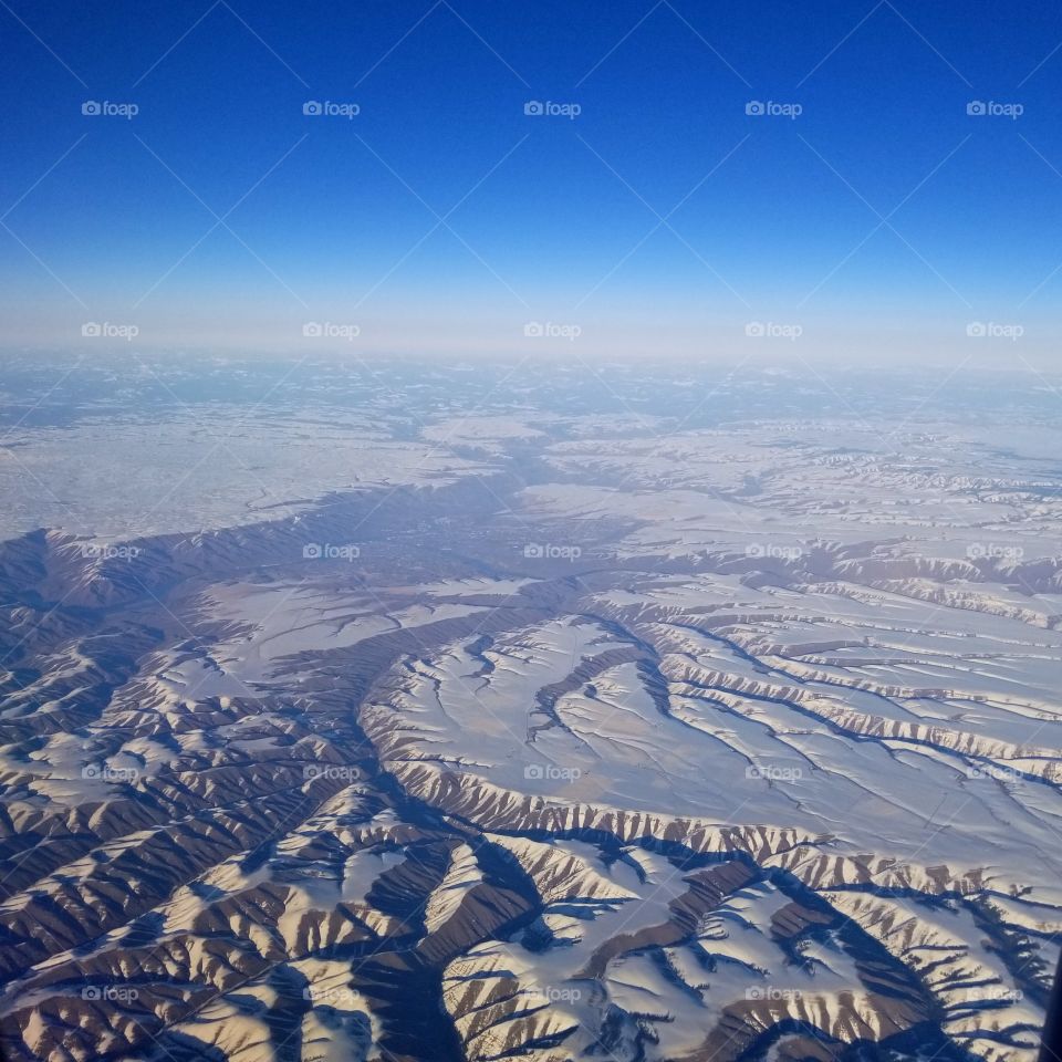 airplane view of snow covered mountain ridges with a blue sky and clouds