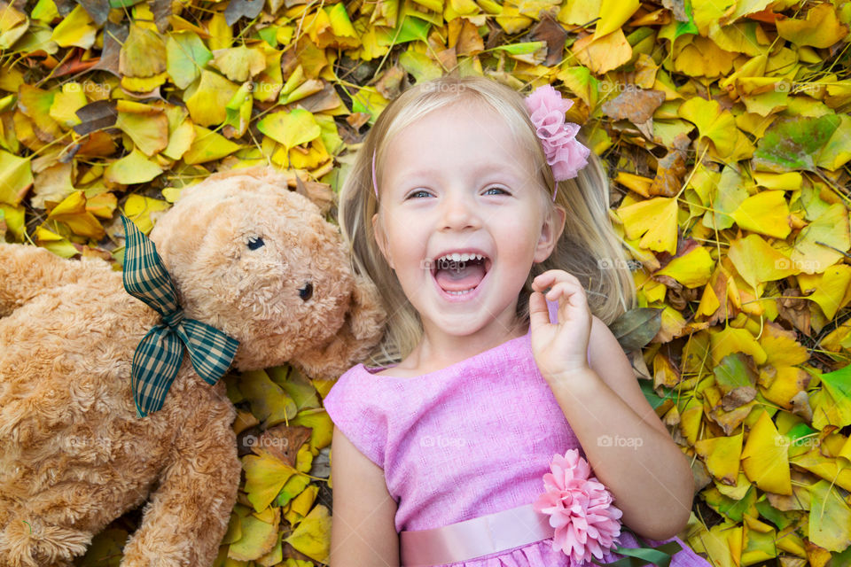 Happy little girl with blonde hair lying on the fallen leaves 