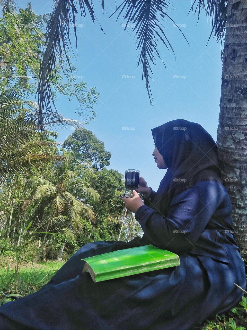 A girl is relaxing under a tree and enjoying the natural scenery around her.