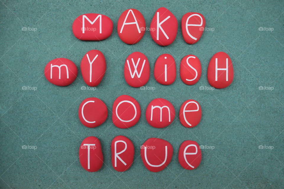 Make my wish come true, positive phrase composed with red colored and carved stone letters over green sand