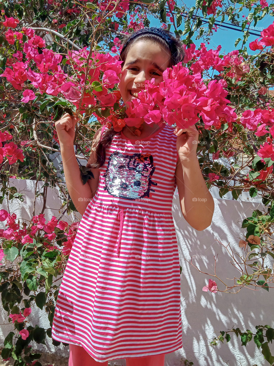 a little girl with a pink clothes standing between pink bougainvillea flowers