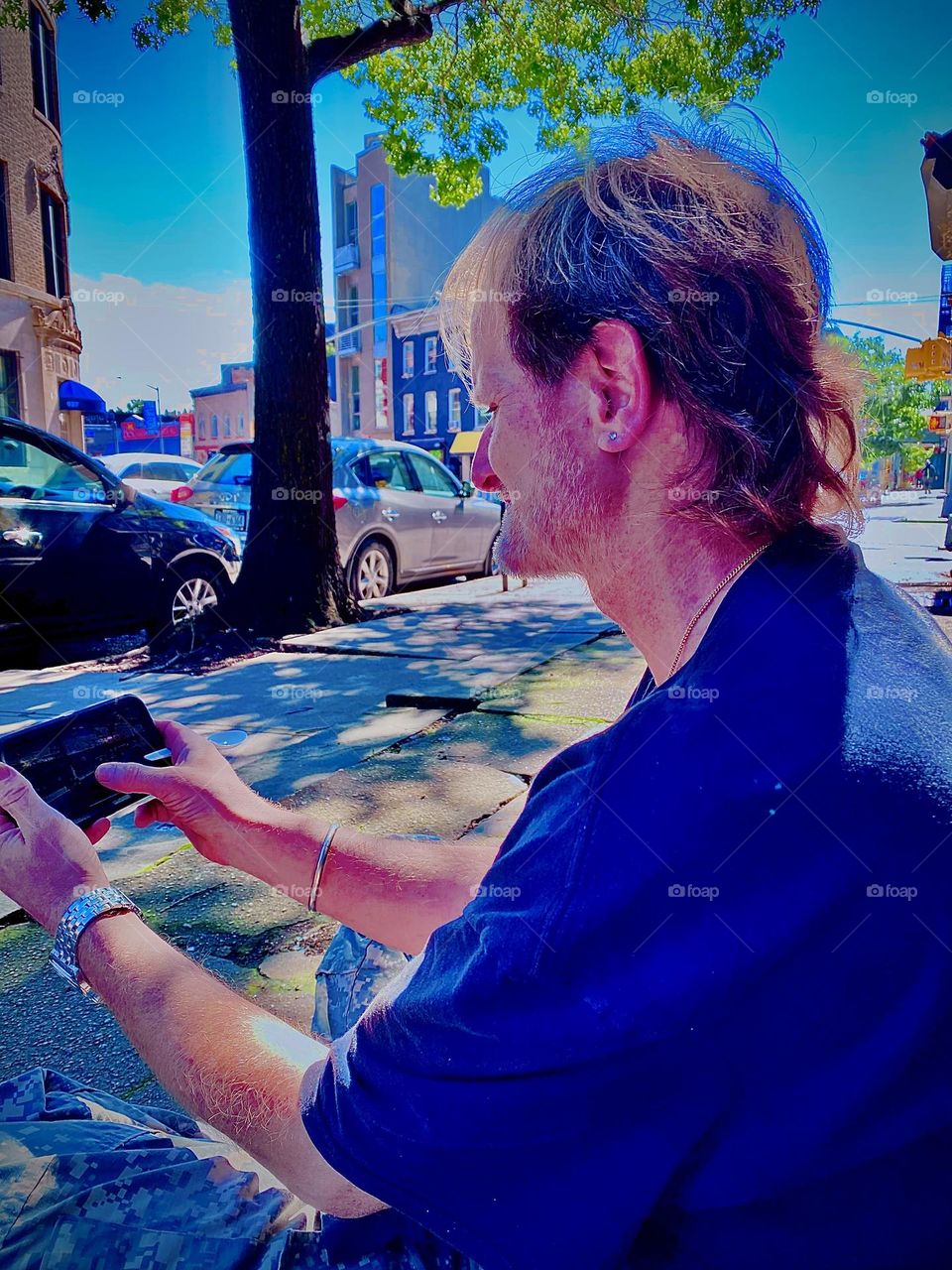 My longtime partner, lover and friend “Timothy Trespas” is sitting on this sun drenched NYC block at “Waverly Av” off “Fulton St” in “Clinton Hill”, Brooklyn playing with his phone. 2023 Hypnotic Productions