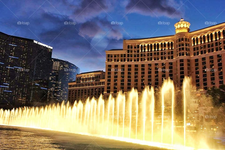 lighted water fountain glowing at night fancy buildings in background